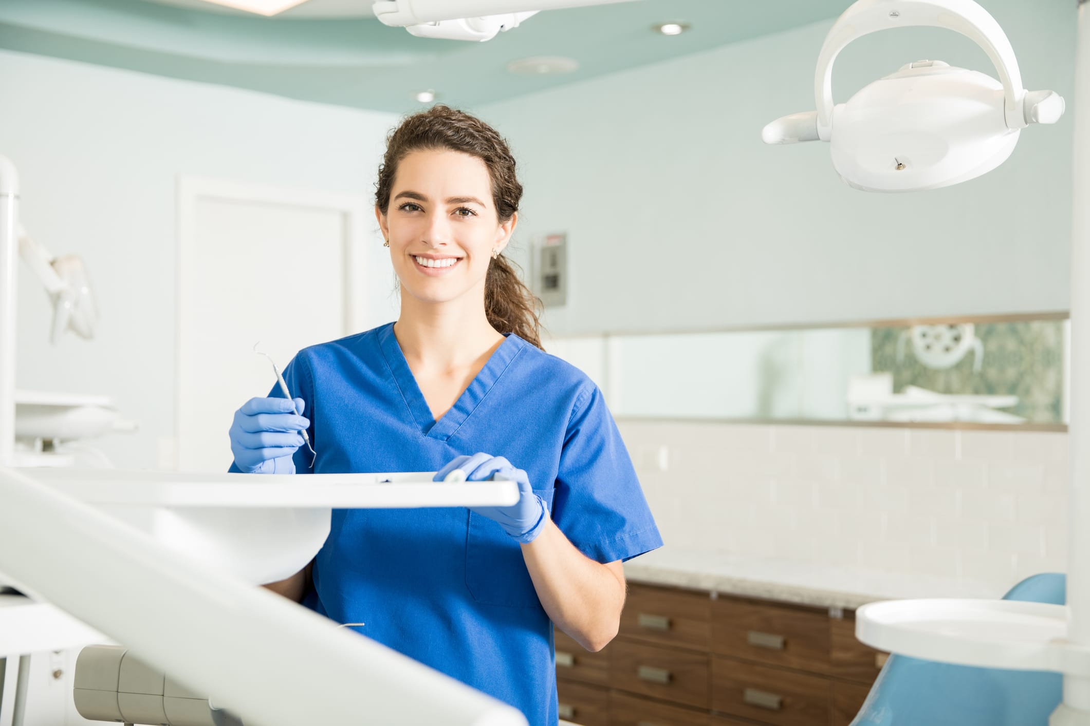 Female dentist in blue scrubs holding tray of tools